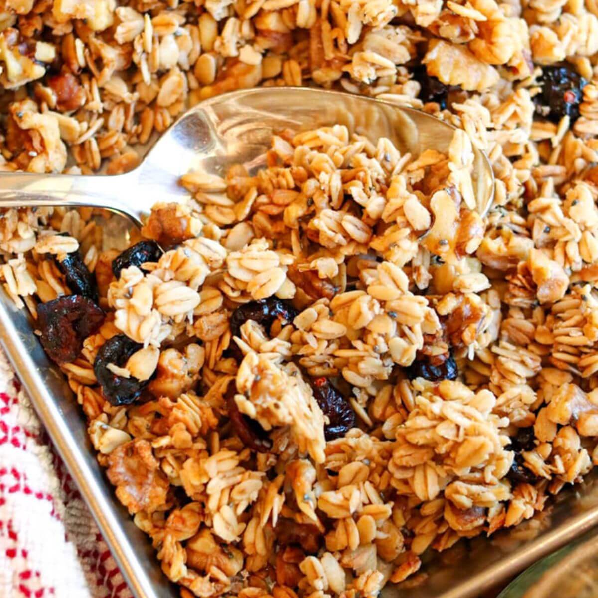 A spoon scooping cinnamon granola off of a baking sheet.
