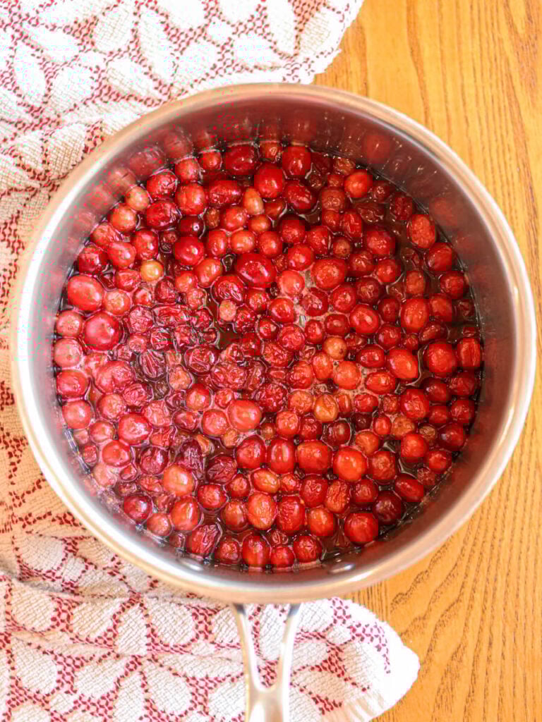 Cranberries, maple syrup, and water simmering in a pot.