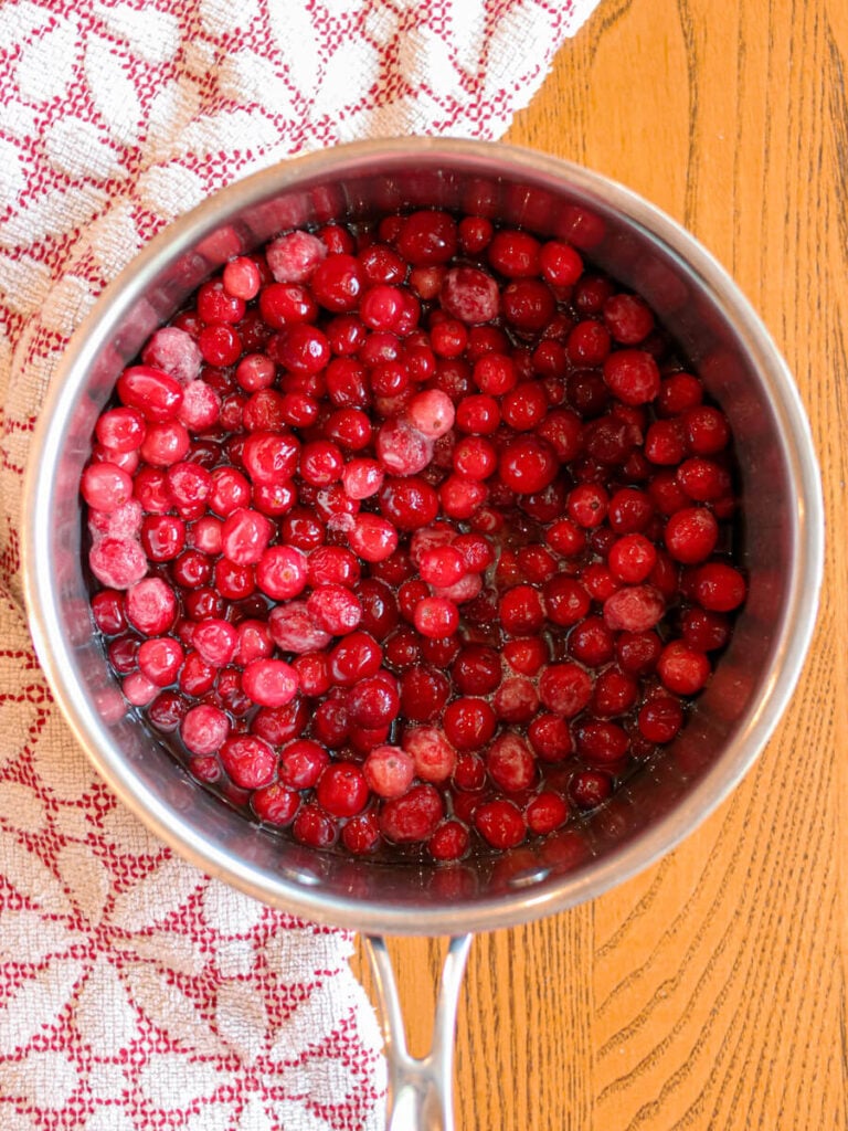 A pot with cranberries, maple syrup, and water on a wooden table.
