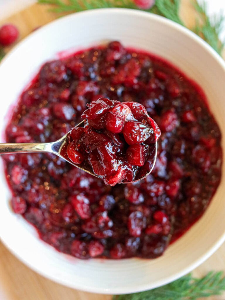 A spoon scooping cranberry sauce out of a white bowl for serving.