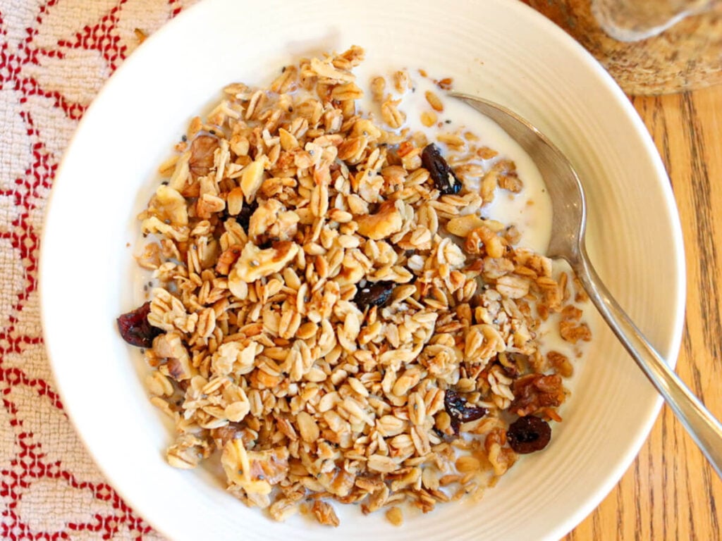 A bowl of homemade low-sugar granola with milk and a spoon.