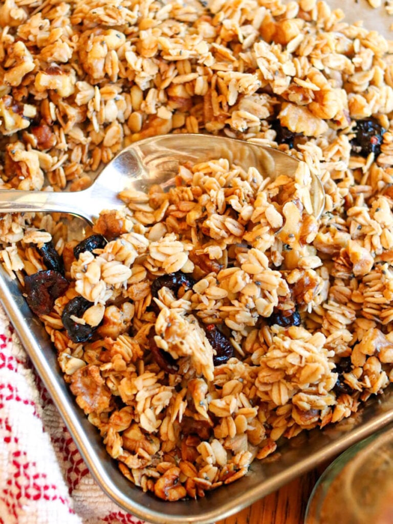 Spoon scooping low-sugar granola on a baking sheet.