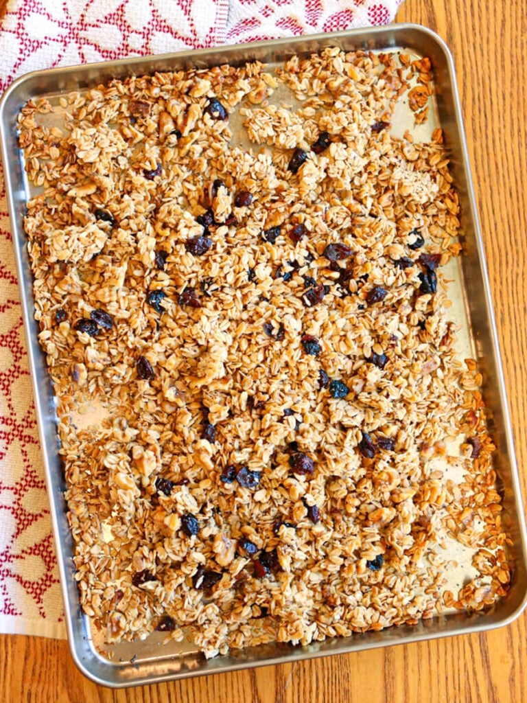 Stirring dried cranberries and chia seeds into homemade granola on a cookie sheet.