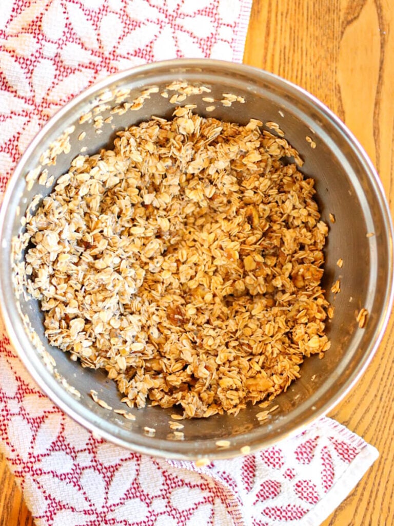 Oats, walnuts, and other ingredients in a mixing bowl on a wood table.