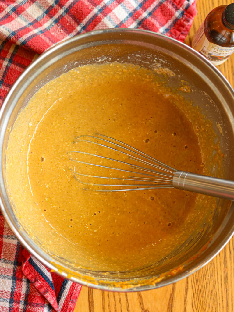 Pumpkin pancake batter in a mixing bowl on a wood table.