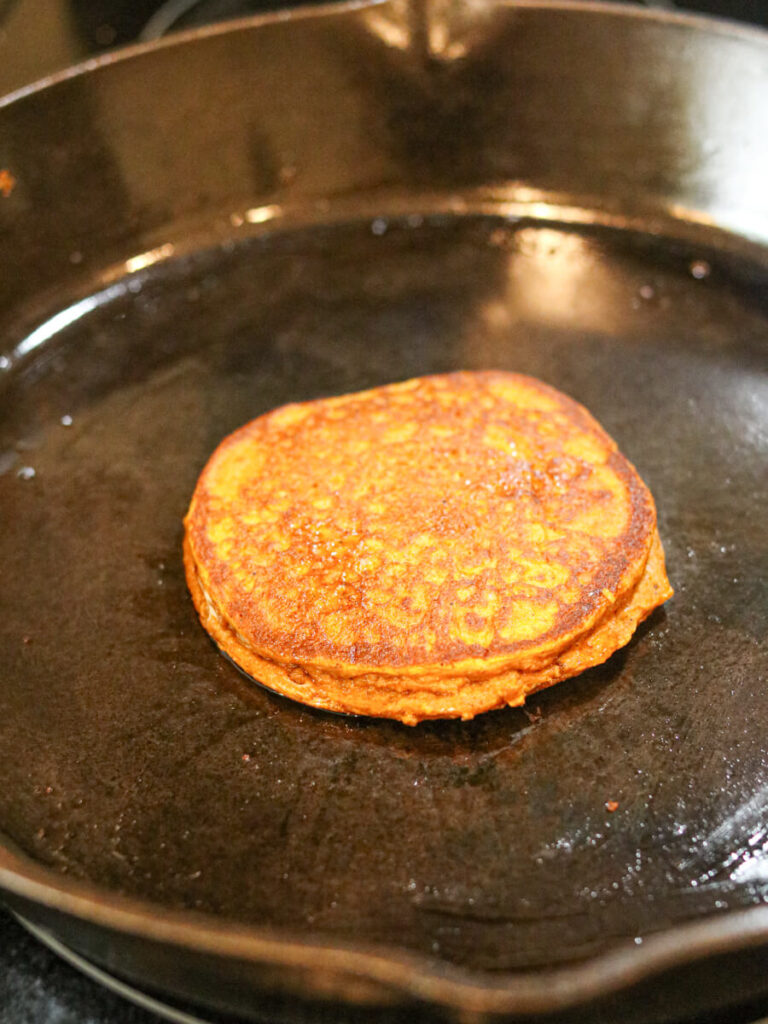 Pumpkin pancake frying in a cast iron skillet.