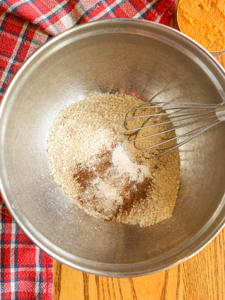 Whisking together oat flour and other dry ingredients in a mixing bowl on a table.