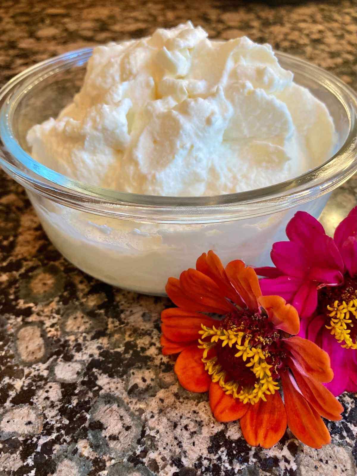 Whipped cream in a glass bowl with two flowers.