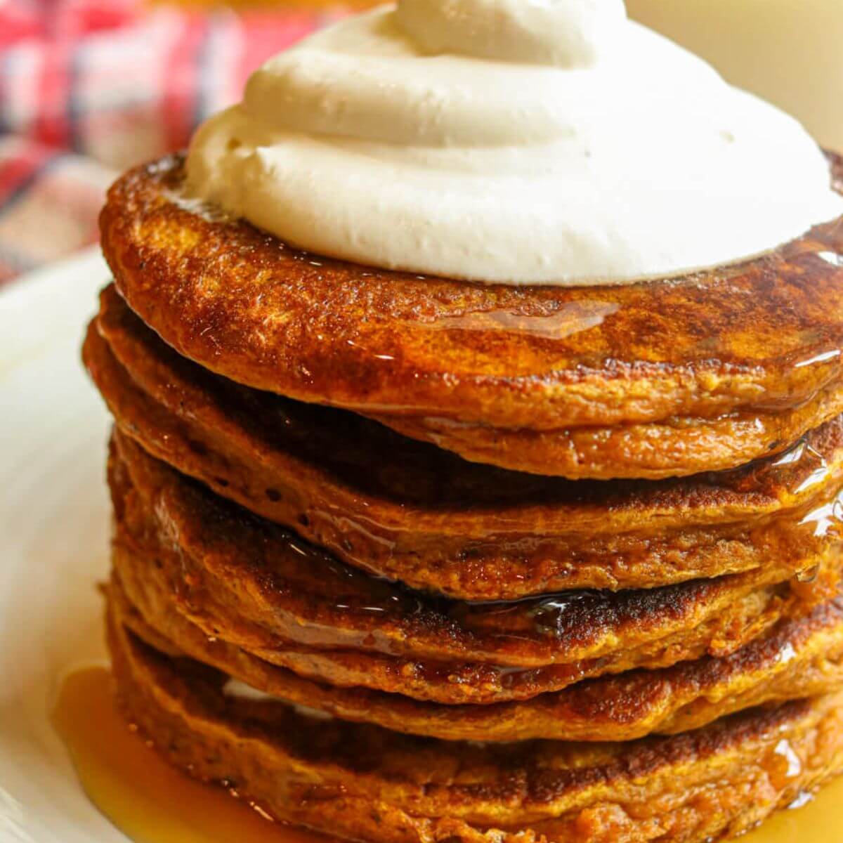 Closeup of stack of oatmeal pumpkin pancakes topped with whipped cream.