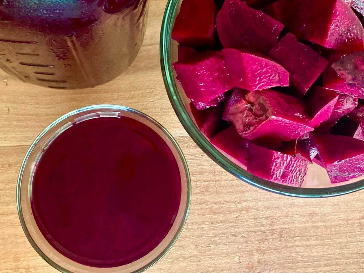 Top view of glass of beet kvass with mason jar filled with beet kvass and bowl of cubed beets.