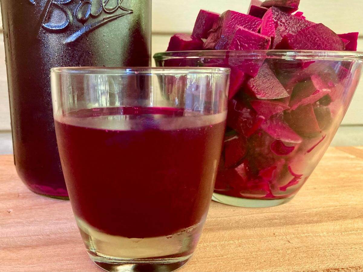 Glass of beet kvass with mason jar filled with beet kvass and bowl of cubed beets.