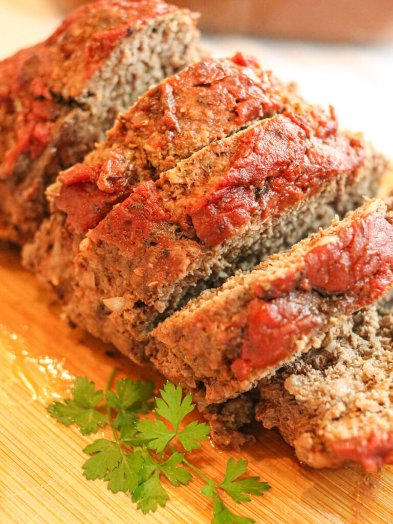 Sliced eggless meatloaf on wooden cutting board with a sprig of parsley.