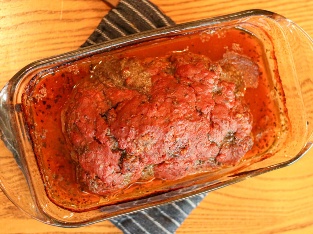 Meatloaf in a glass pan just out of the oven on a hotbed on a wooden table.