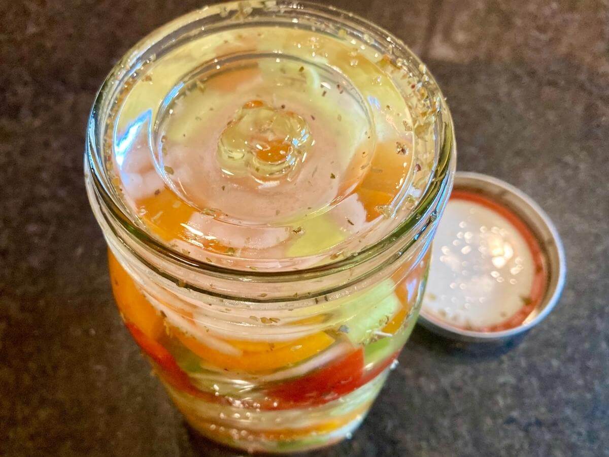 Jar with peppers and onions under a fermentation weight.