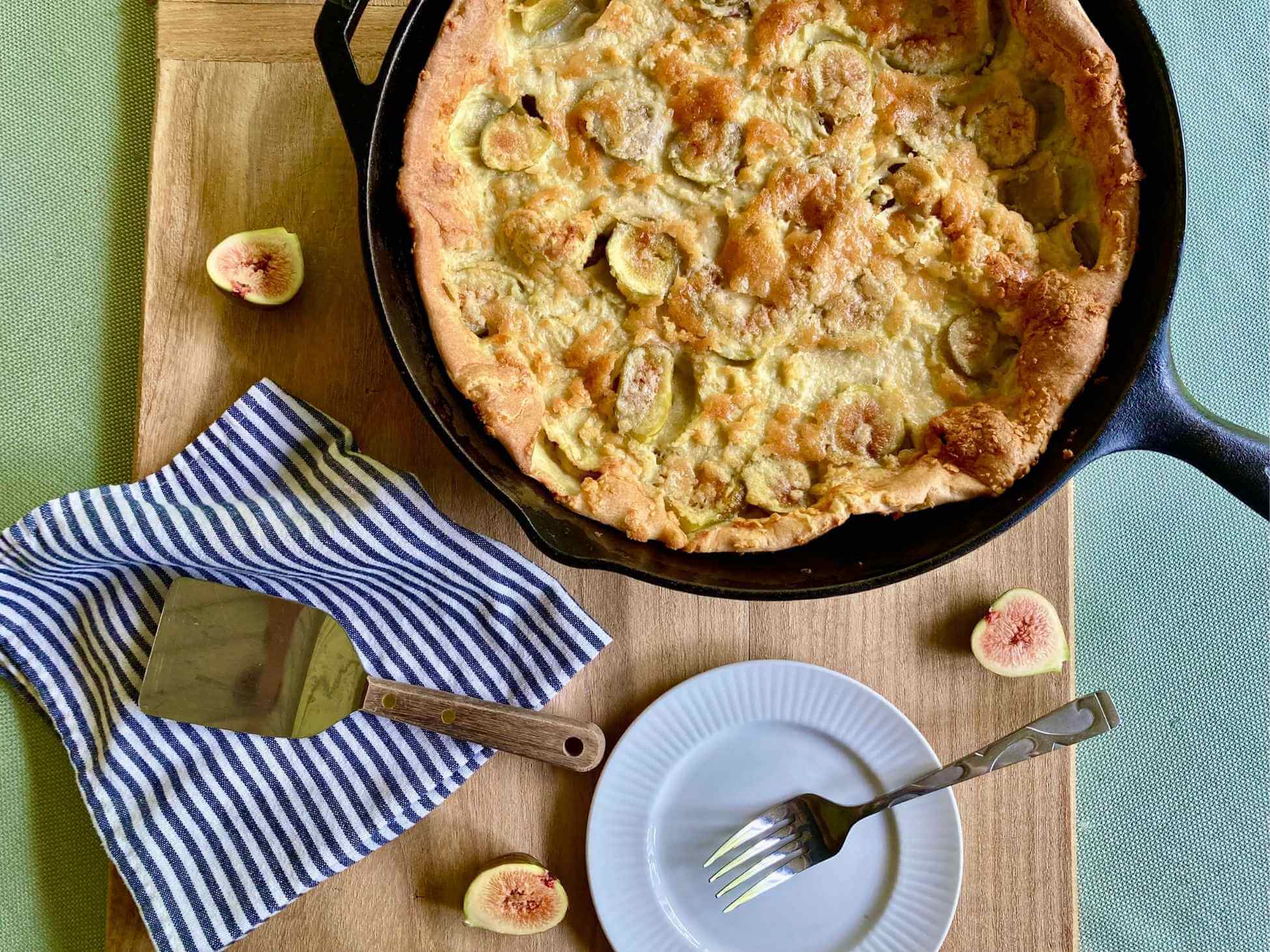 Fig Dutch baby in a cast iron skillet with a plate and spatula.
