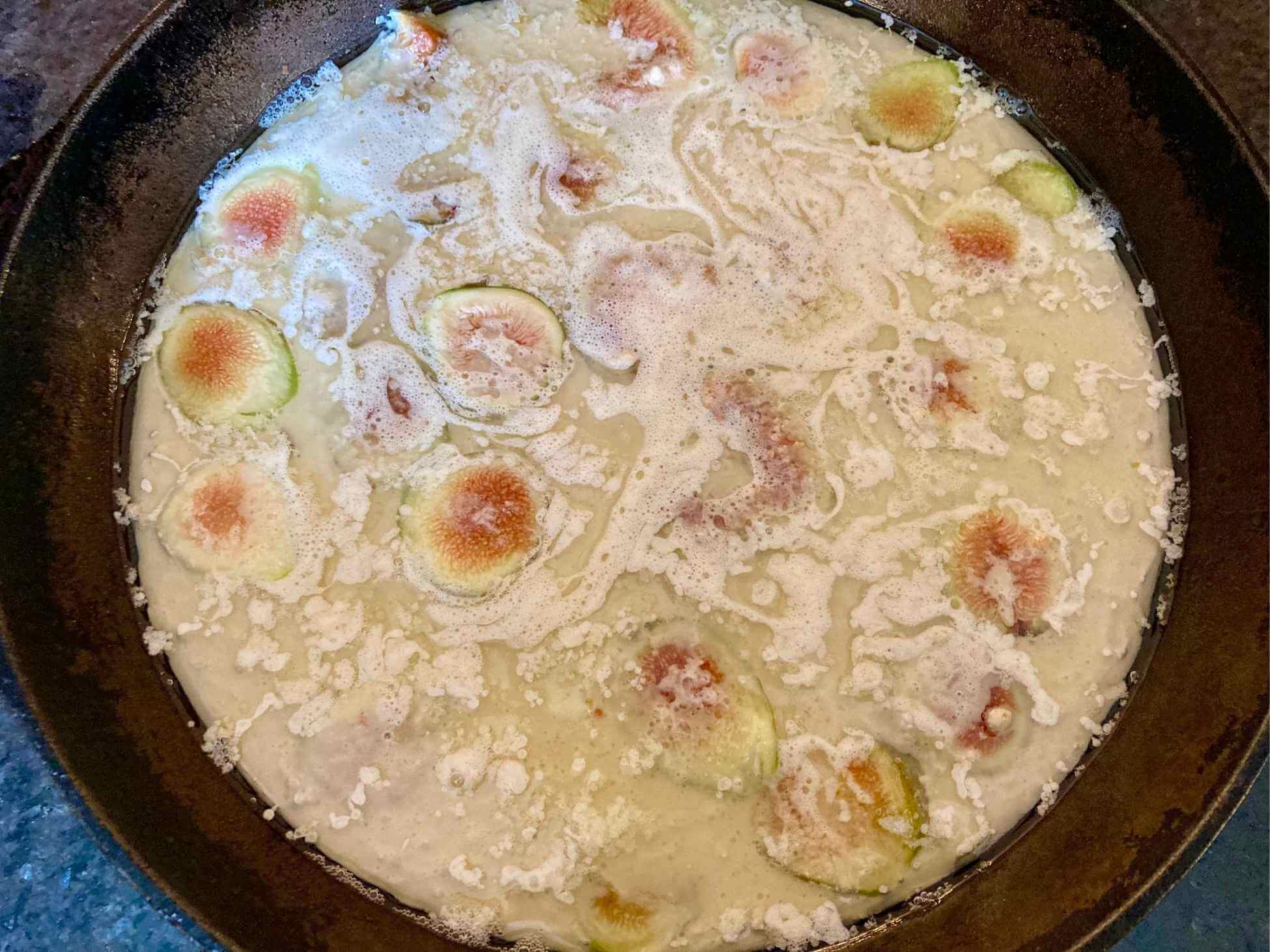 Unbaked fig Dutch baby in a cast iron skillet.