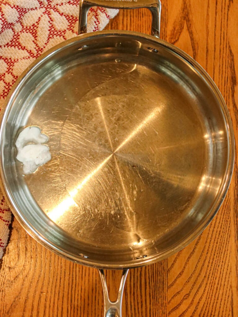 Coconut oil melting in a saute pan on a wood table.
