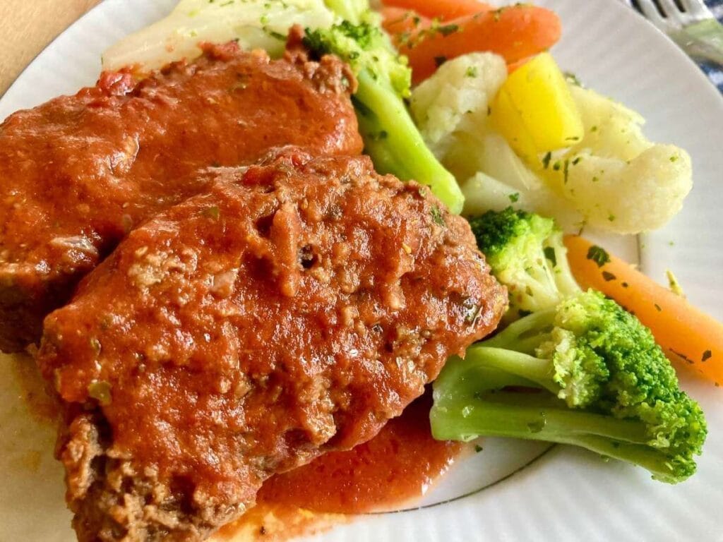 2 slices of gluten-free meatloaf on a plate with steamed vegetables.