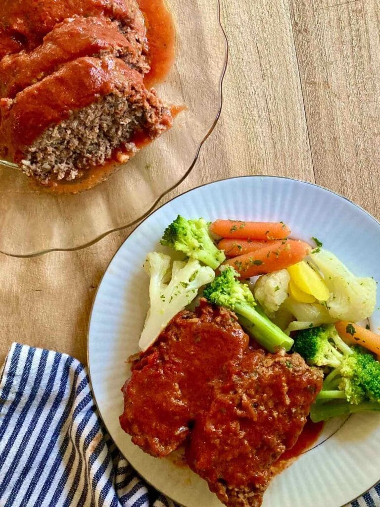 Sliced meatloaf on a serving platter and on a plate with vegetables.