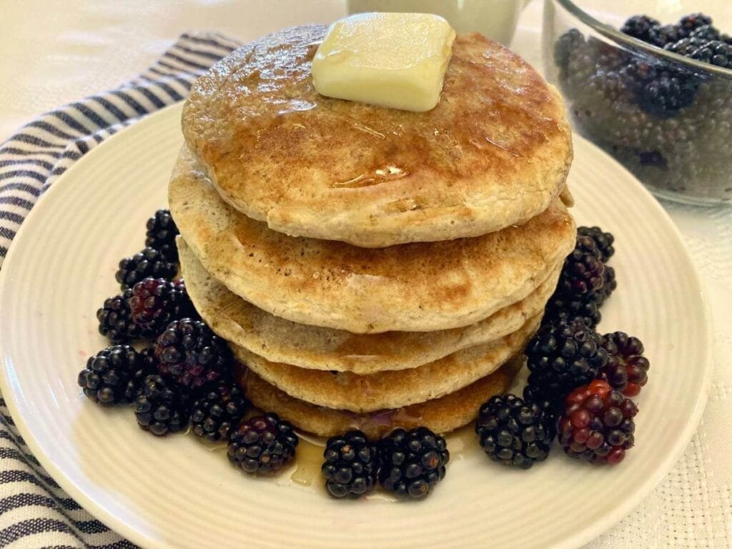 Stack of gluten-free oat flour pancakes with butter and blackberries on a plate.