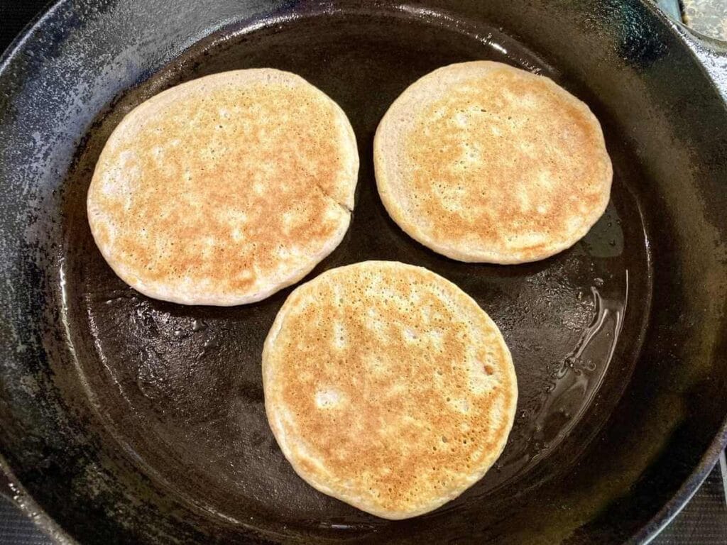 Three pancakes frying in a skillet.