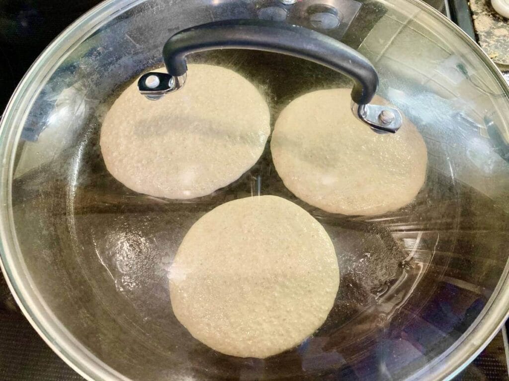 Frying three pancakes in a skillet with the lid on.