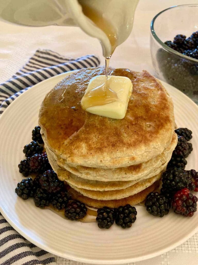 Pouring syrup on a stack of gluten-free oat flour pancakes.
