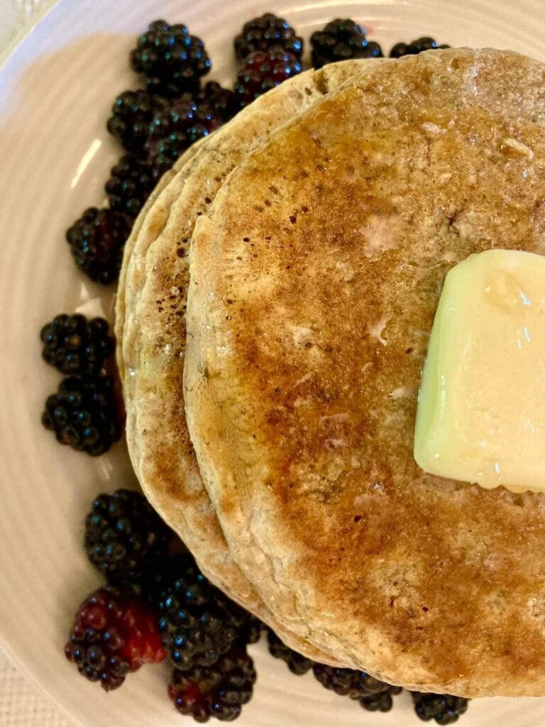 Closeup of stack of gluten-free oat flour pancakes with butter and blackberries.