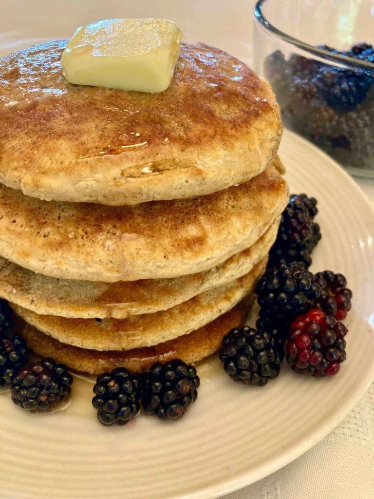 Stack of gluten-free oat flour pancakes with butter and fresh blackberries on a plate.