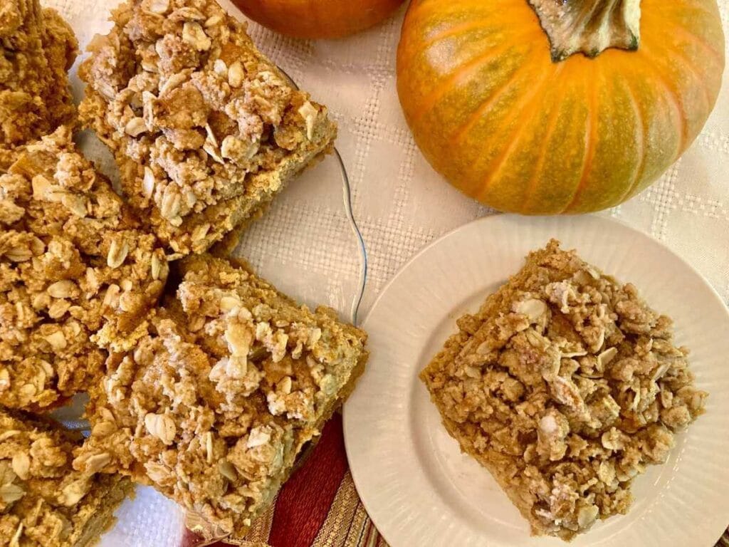 Gluten-free pumpkin cheesecake bars on a serving platter and one on a plate.
