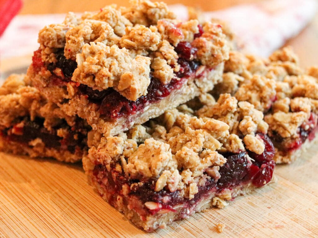 Gluten-free cranberry bars stacked on a wooden cutting board.