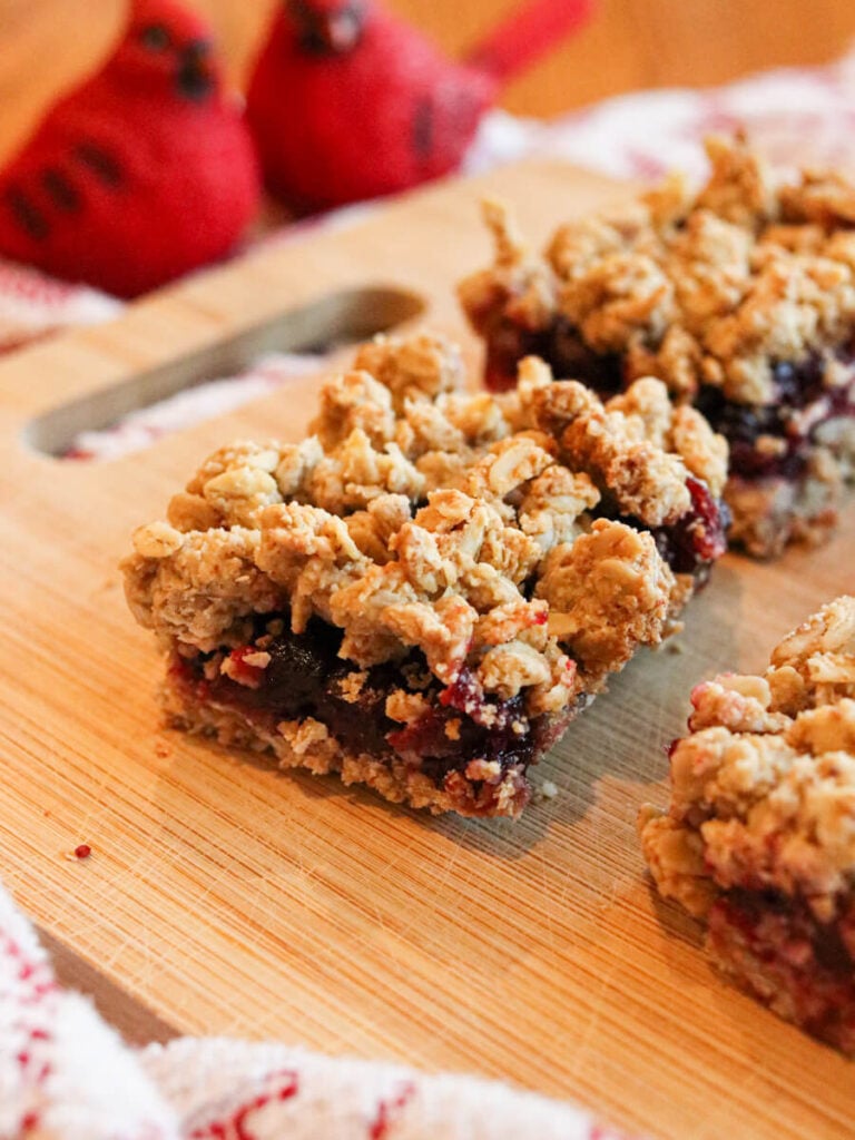 A cranberry crisp bar on a wood cutting board with cardinal bird decorations in the background.