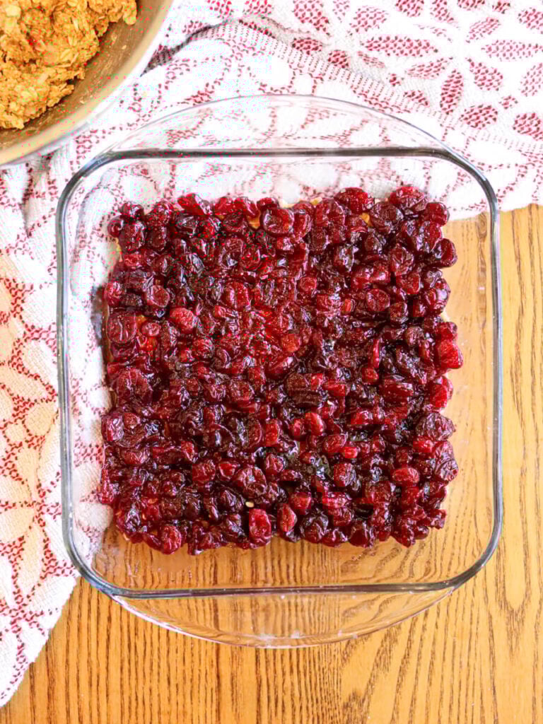 Cranberry sauce spread over crust in a glass baking dish on a wooden table.