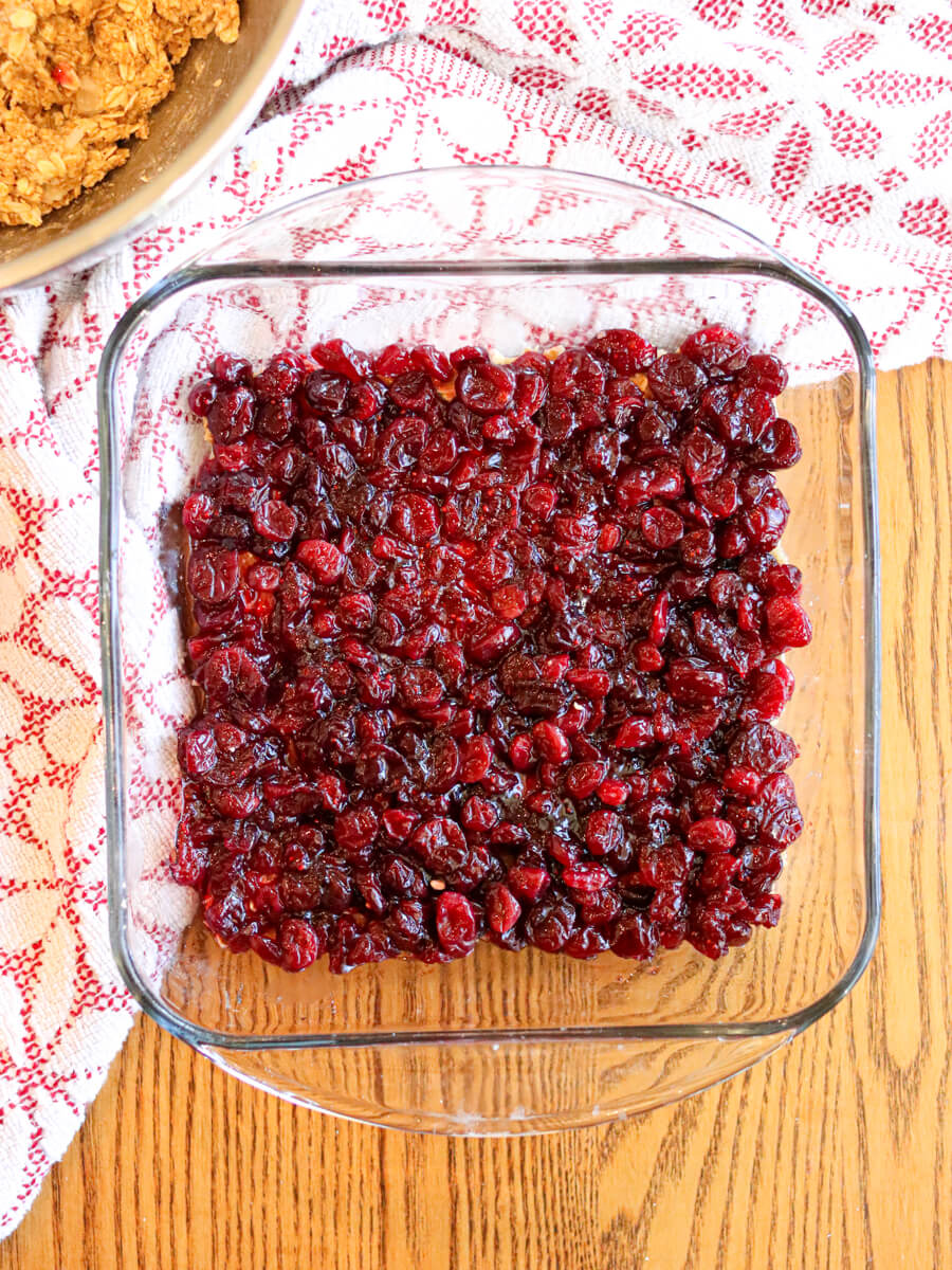 Cranberry sauce spread over crust in a glass baking dish on a wooden table.