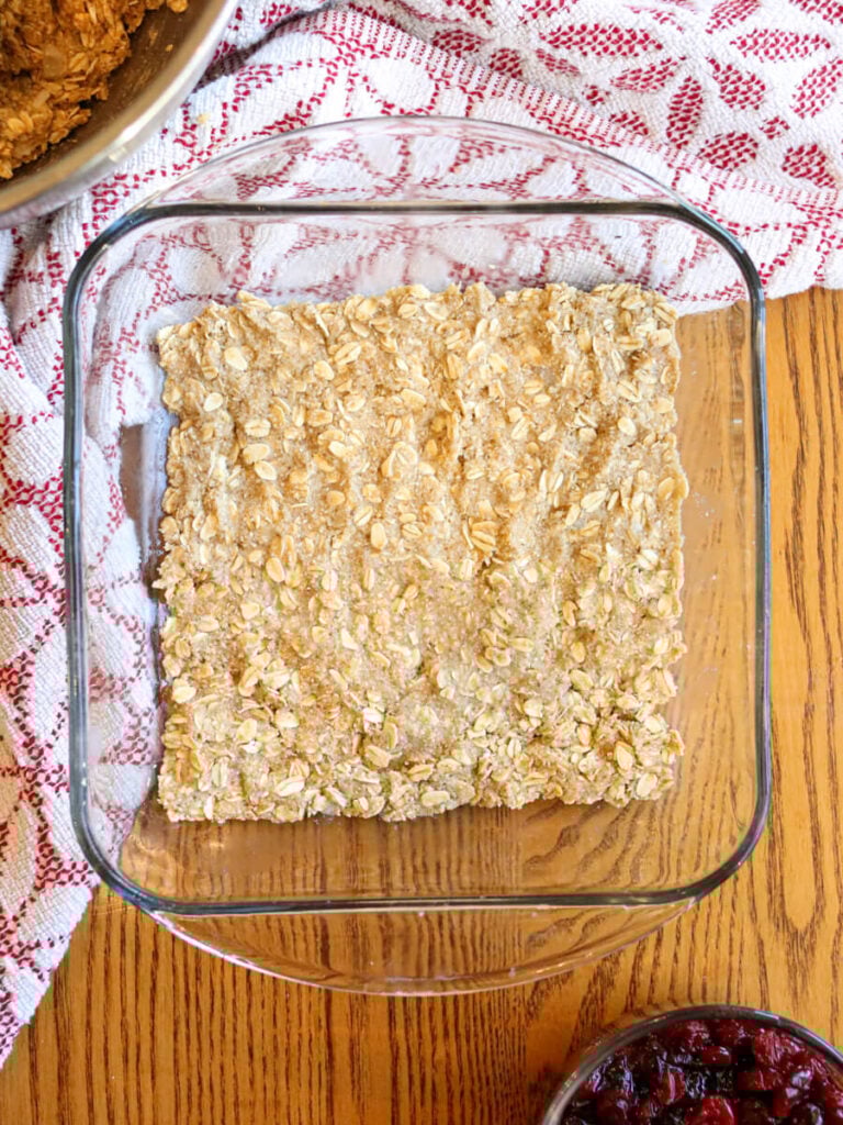 Oat crust pressed into the bottom of a square glass baking dish on a wooden table.