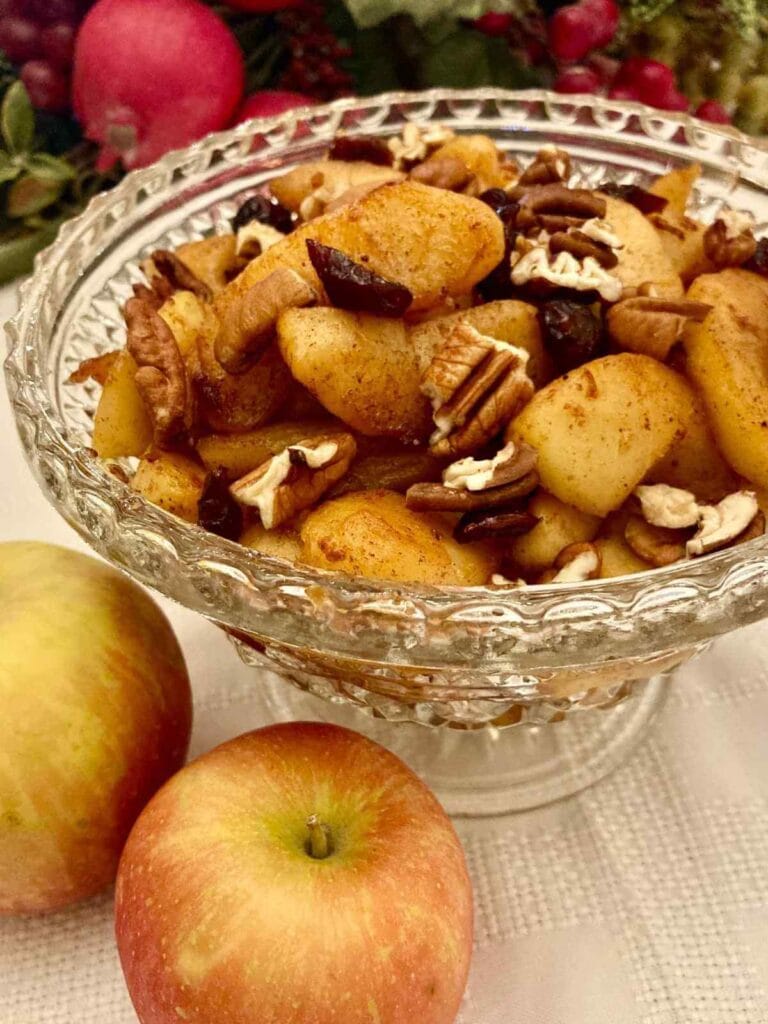 Healthy fried apples in a serving dish with 2 fresh apples beside it.