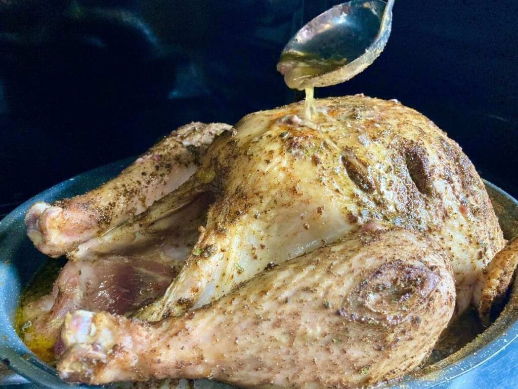Basting a turkey in the oven with a ladle.