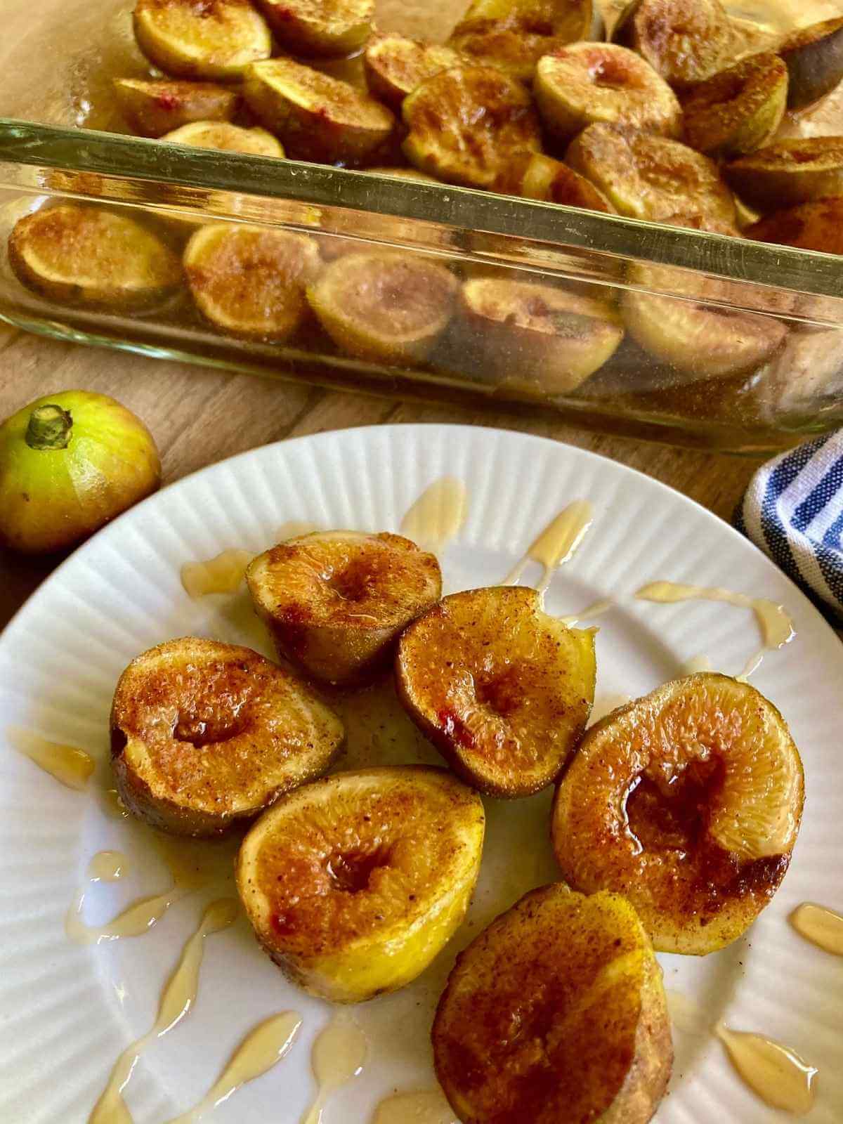 Roasted figs on a plate drizzled with honey with a baking dish in the background.