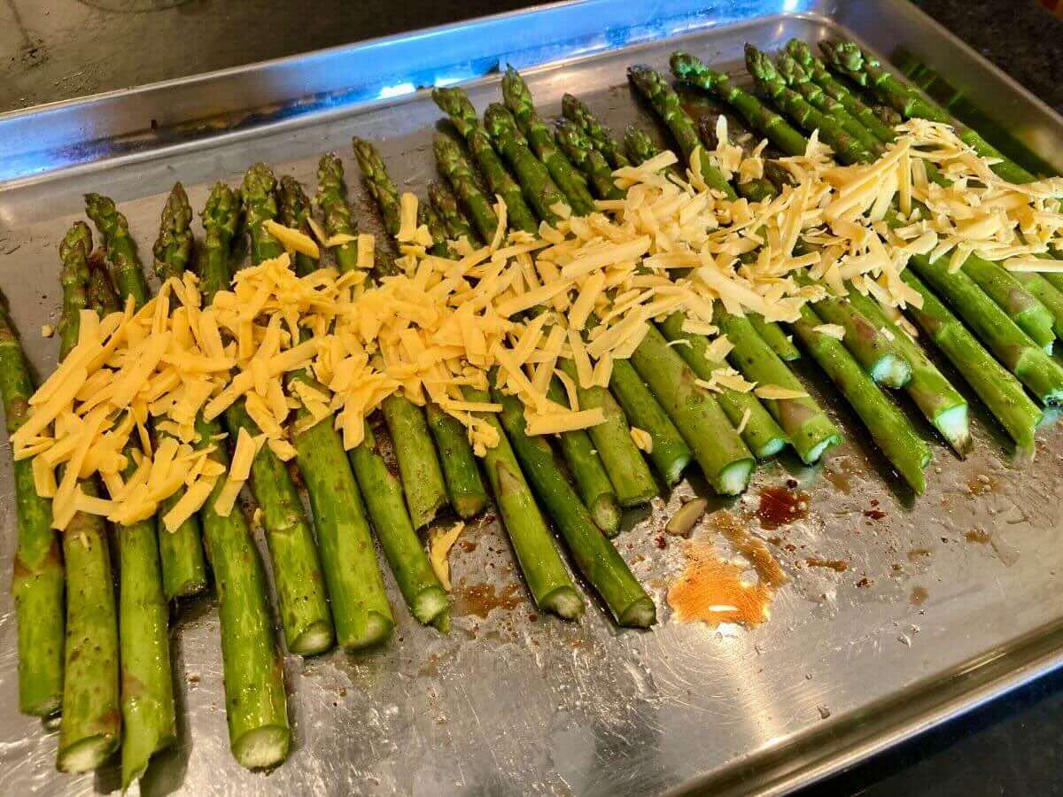 Asparagus with shredded cheese on baking sheet