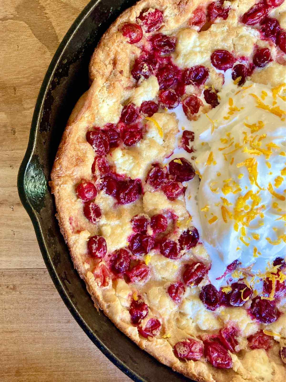 half of cranberry cheesecake dutch baby with whipped cream in skillet