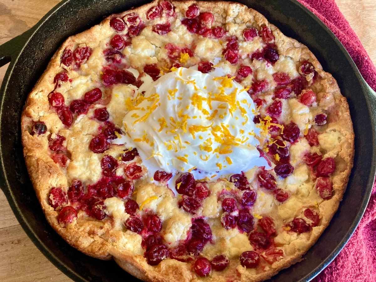 cranberry cheesecake dutch baby in skillet with whipped cream