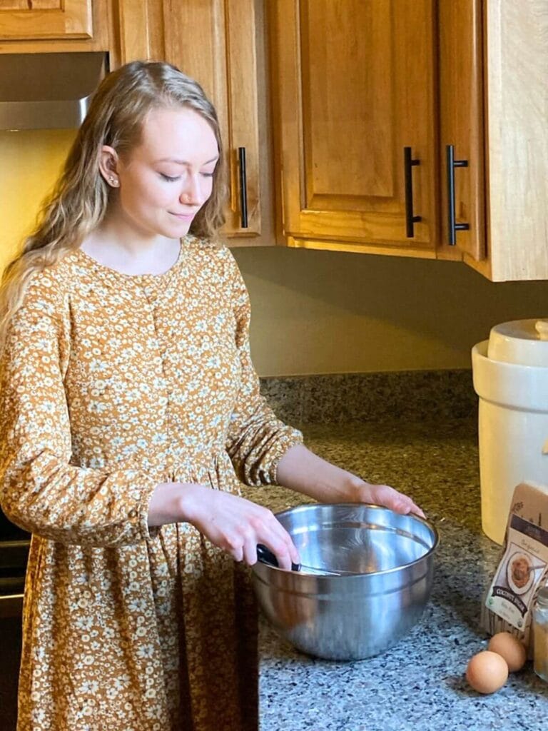 Woman standing in a kitchen cooking food and mixing ingredients in a bowl.