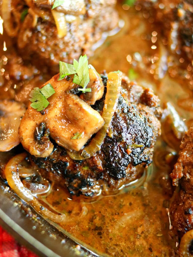 Gluten-free Salisbury steak patty in gravy with mushroom and onion slices on top.