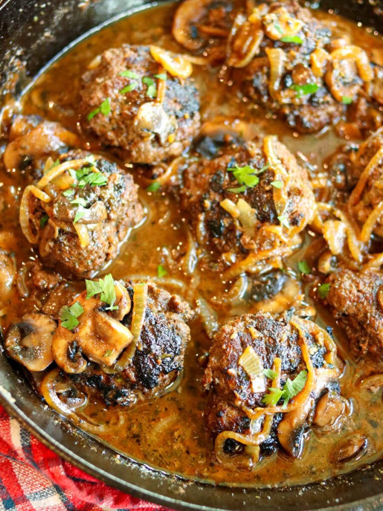Closeup view of juicy Salisbury steak patties smothered in a mushroom and onion gravy in a skillet.