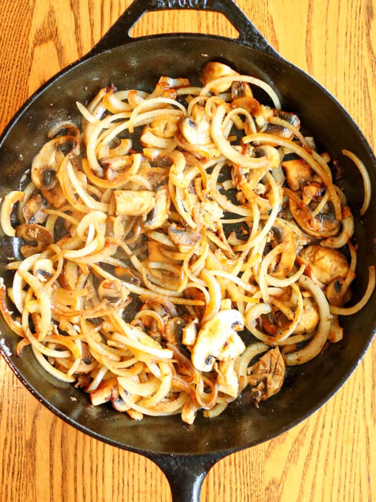 Sliced onions, mushrooms, and garlic sautéing in a cast iron skillet.