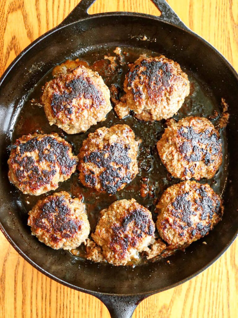 Beef patties searing in a cast iron skillet.
