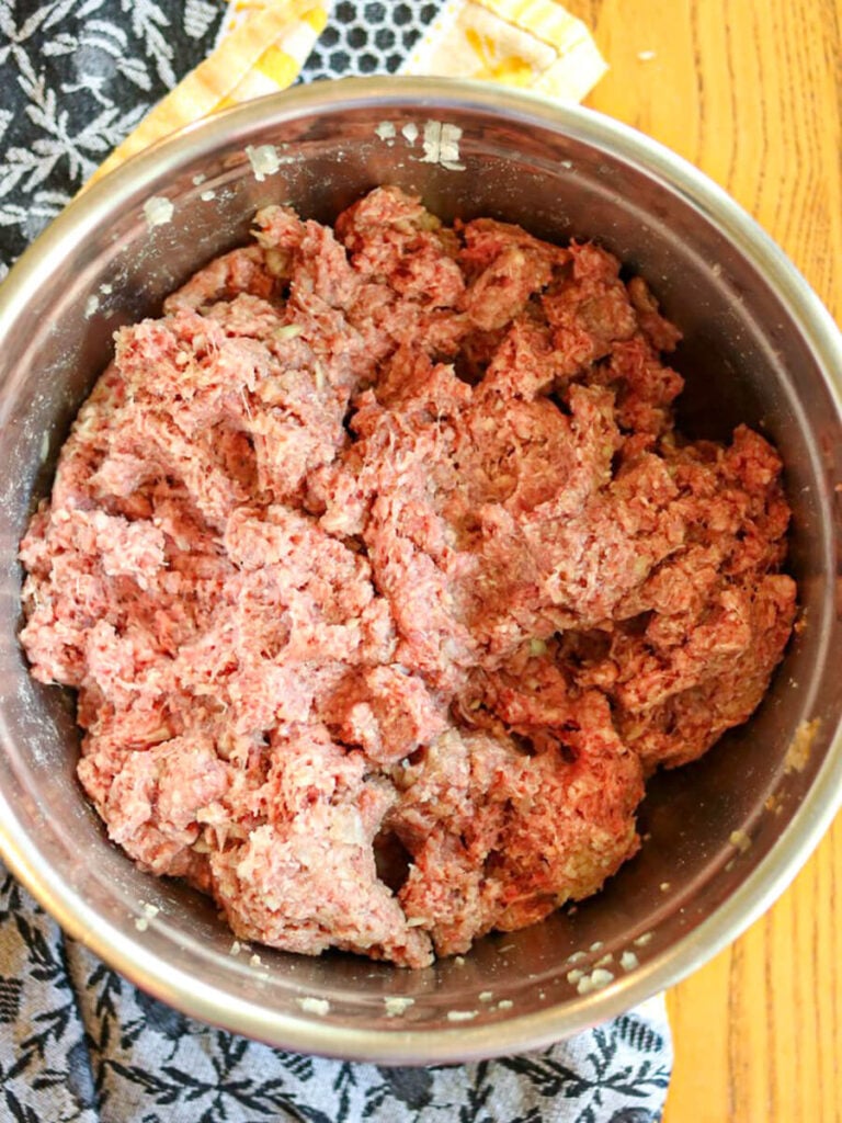 Meat mixture in a stainless steel bowl beside a decorative blue and yellow kitchen towel.