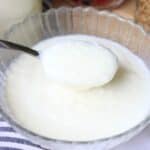 A spoonful of creamy, white yogurt made from raw milk is held above a glass bowl.