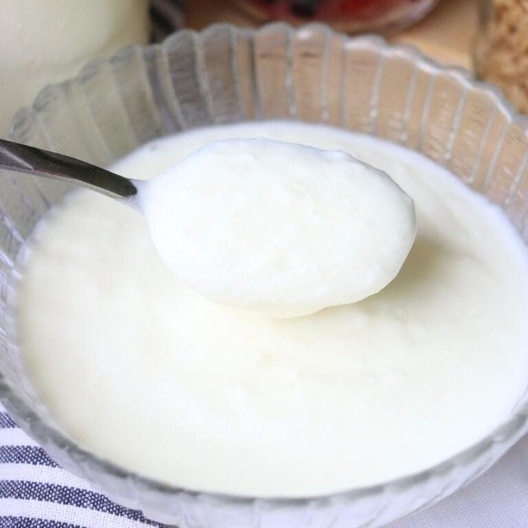 A spoonful of creamy, white yogurt made from raw milk is held above a glass bowl.
