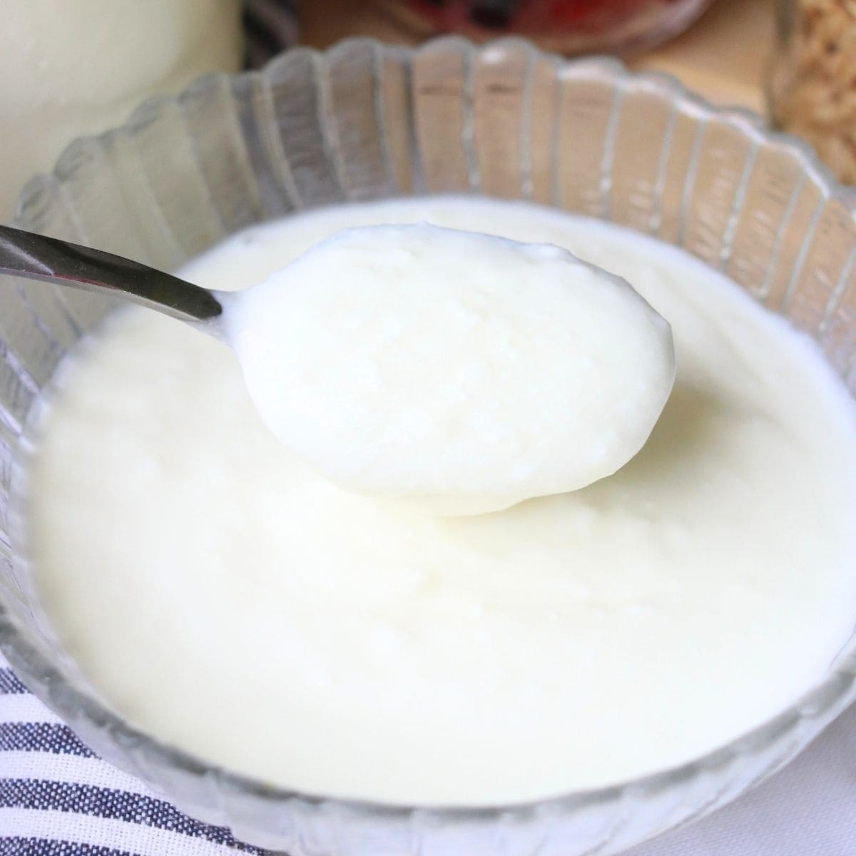 A spoonful of creamy, white yogurt made from raw milk is held above a glass bowl.